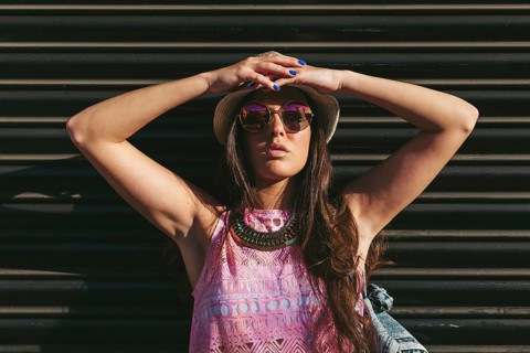 Stylish woman posing outdoors wearing a summer hat and sunglasses. Her colorful outfit and