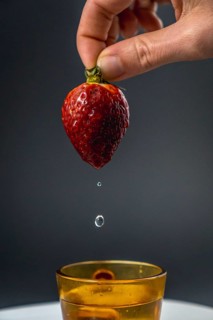 A nice water wet strawberry held by a woman's hand with black background