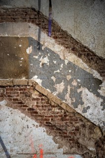 A close-up of an old wall under renovation, revealing layers of peeling plaster and exposed brick.