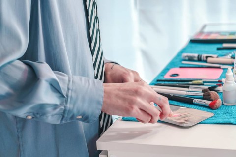 Makeup artist in a stylish blue shirt and striped tie preparing foundation on a metal palette with
