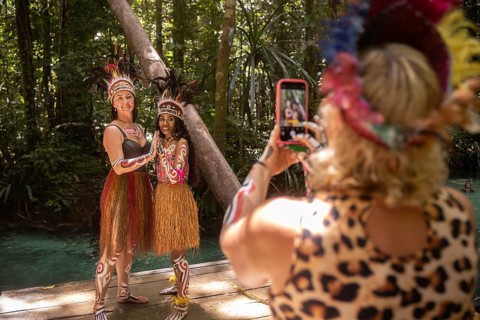 Tourist takes a photo of a friend posing with a Pacific Islander in traditional dress, deep in the
