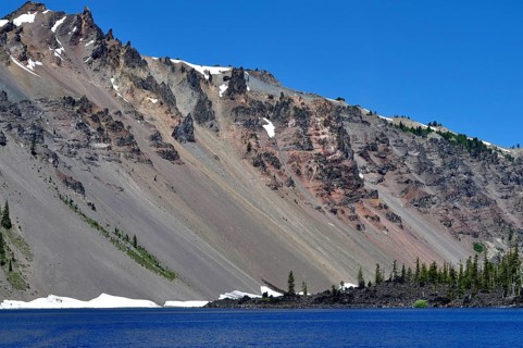 Mountain slope with snow and rock formations over a blue lake, Crater Lake National Park, Oregon,