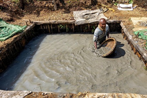 A man stands in a mud pit and holds a loaded basket, the sapphire and gemstone mines at Ratnapura