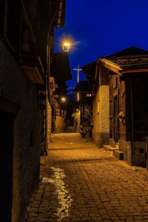 Old illuminated farmhouses in Rue Du Village, night view, historic town center, Grimentz, Val