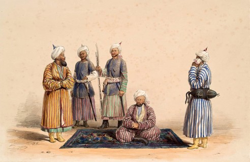 Five men in traditional clothing gather around a rug