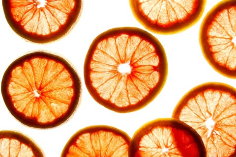 Bright, translucent slices of citrus fruit are back lit on a light background, highlighting their