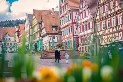 Lively scene with people in front of colorful half-timbered houses and a central fountain, Calw,