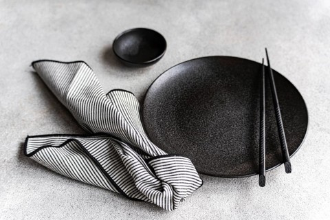 A sophisticated black and white table setting with a round black plate, chopsticks, and a striped