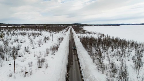 A stunning aerial view captures a long, straight road cutting through a snow-covered nordic