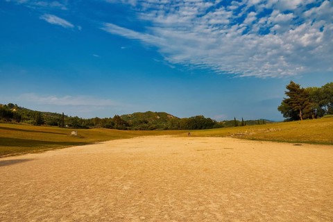 Ancient stadium, wide open field under a vast sky surrounded by light forest, Archaeological Site,