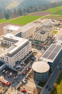 Modern building with a gathering of people in sunlight, surrounded by fields, new hospital at the