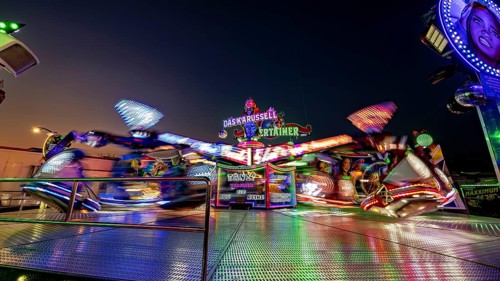 Colourfully illuminated carousel in quick turn at night at a fair, carousel and hustle and bustle