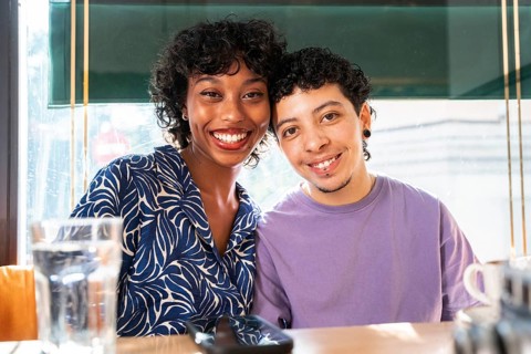 A smiling multiethnic LGBTQ+ couple enjoys a relaxed moment at a cozy café. They sit closely