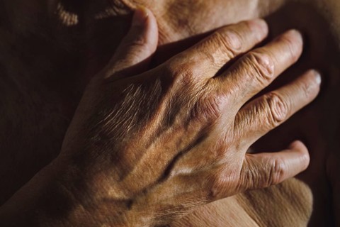 A detailed view of a senior man's hand resting on his chest, showcasing wrinkles and texture The
