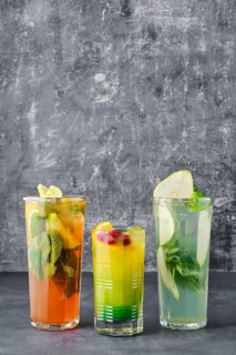 Three glasses with fruit refreshing drink on gray shabby background