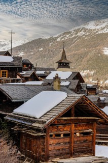 Snow-covered roofs of old farmhouses and barn storage, behind the church tower of the Saint