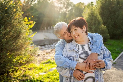 An elderly couple shares a loving embrace, dressed casually, with smiles on their faces. They enjoy
