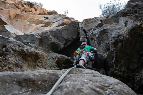 A climber in harness and helmet navigates a challenging natural rock face, displaying skill and