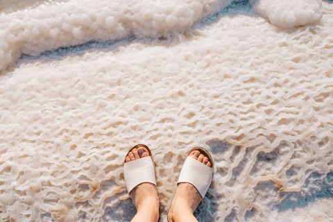 Cropped unrecognizable view of a person's feet in white sandals standing on the textured salt