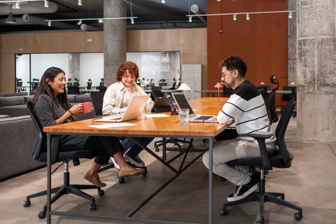 A diverse group of coworkers engaging in teamwork around a large wooden table in a modern office