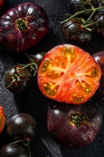 Close up of fresh black tomatoes with a vibrant red interior, glistening with water droplets. The
