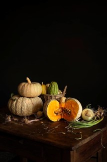 A rustic still life featuring pumpkins, root vegetables, and a basket of gourds on a wooden table.