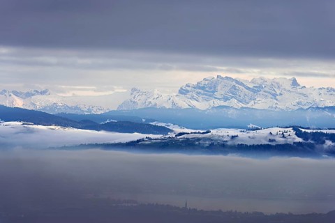 Fog over Lake Zug in the foreground the village of Cham, behind the snow-covered Alps with the