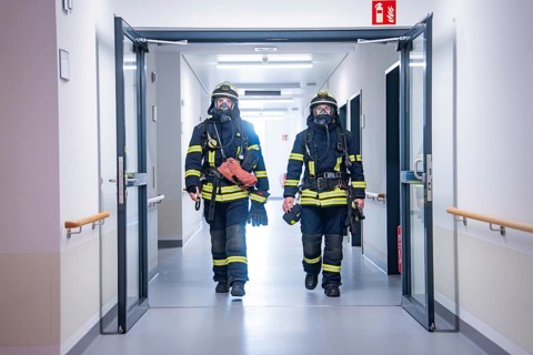 Two firefighters with full equipment and respiratory protection in the corridor, fire brigade