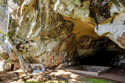 Large rock overhang with shady area, altar on the wall, The Batadombalena cave temple near