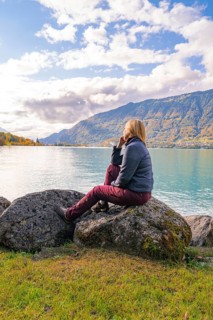 Woman sitting on rocks and looking at the lake with mountains in the background, Lake Brienz,