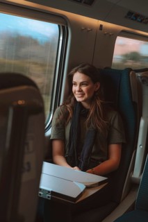 A woman smiles warmly while sitting by a window on a European train. She enjoys the passing