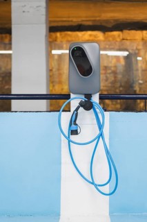 A modern electric vehicle (EV) charging station, equipped with a blue charging cable, set against a