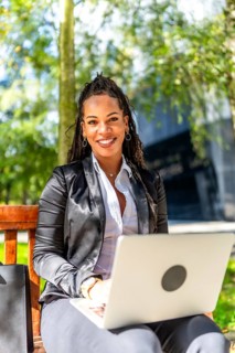 Vertical portrait of a latin businesswoman using laptop sitting on a park bench