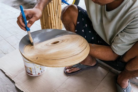 A Balinese artisan carefully paints a wooden sculpture using grey hues. His focus and craftsmanship