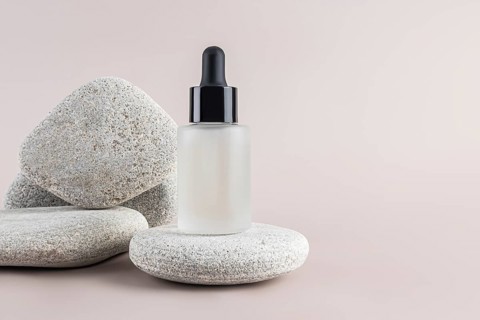 A sleek dropper bottle with frosted glass, elegantly displayed on smooth stones against a neutral