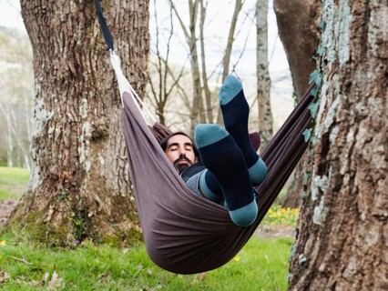 A man peacefully rests in a hammock suspended between trees in a serene forest setting. Surrounded