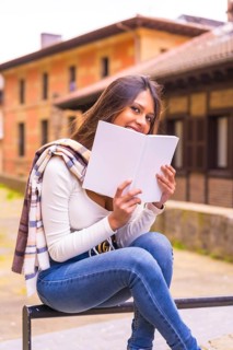 A young Latin woman with a white t-shirt, jeans and a scarf enjoying and imagining reading a book,