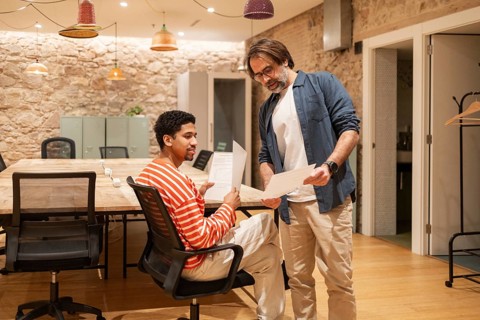 Two colleagues collaborate in a cozy coworking space with a rustic design. They discuss documents,
