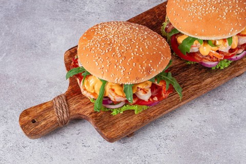 Two shrimp burgers and buns with sesame seeds, bacon, lettuce, tomatoes and onions, On a wooden