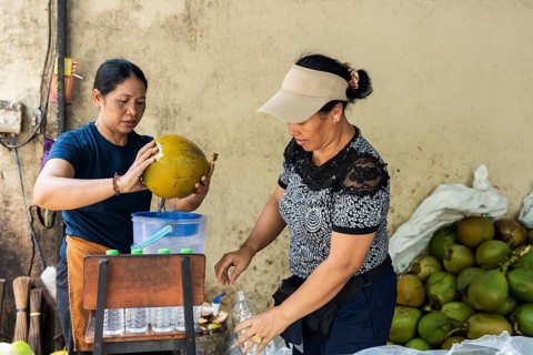 Two asian women expertly open a coconut to extract refreshing coconut water, pouring it into