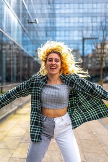 Carefree young woman dancing with flowing hair and open arms, enjoying urban music in a modern city