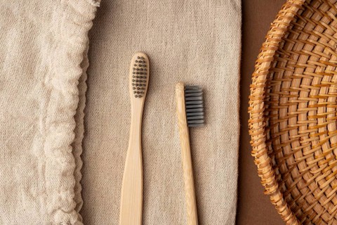 Top view of two bamboo toothbrushes on a textured burlap background, accompanied by a woven basket