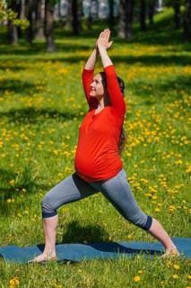 Pregnancy yoga exercise, pregnant woman doing yoga asana Virabhadrasana warrior pose outdoors on