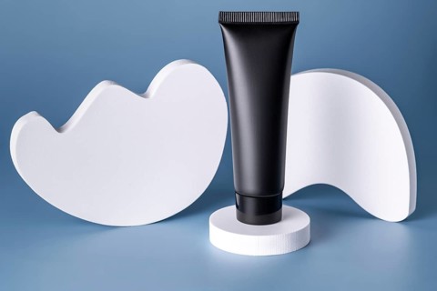 A sleek, black cosmetic tube elegantly displayed on a white circular podium against a soft blue