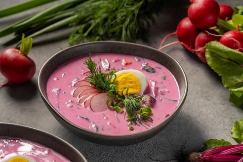 A bowl of chilled beetroot soup garnished with sliced radish, fresh dill, and a halved boiled egg.