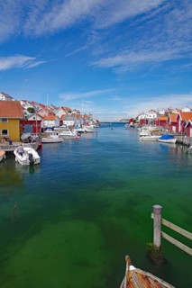 Wooden houses on the water with boats, blue sky with clouds shows a peaceful harbour atmosphere,