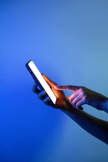 A hand delicately touches a smartphone screen, set aglow by vivid neon lights. The image captures