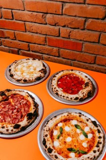 A variety of wood-fired pizzas served on metal plates: Four Cheese with creamy sauce, Margherita