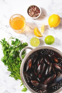 Fresh mussels, in a metal colander, with ingredients on the table, light background, no people