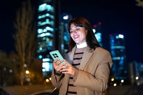 Young woman smiling as she checks her smartphone, screen glow lighting her face against blurred